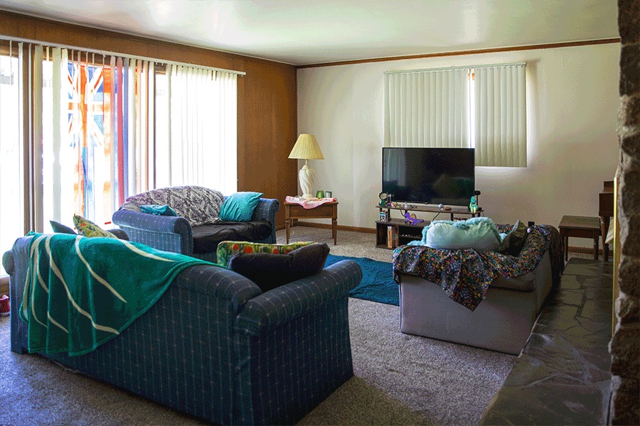 A cozy living room with three sofas, a TV, large sliding glass doors and windows with blinds, and a fireplace.